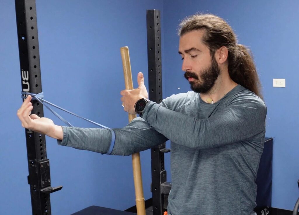 Dr. John with the band around his forearm and the dowel at his bicep getting ready for his banded mobility exercise to eliminate elbow pain